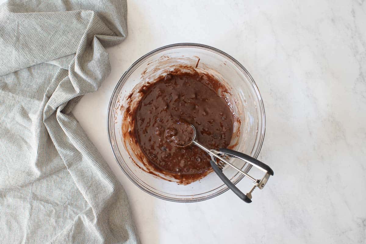 Wet chocolate cookie batter in bowl with cookie scoop.