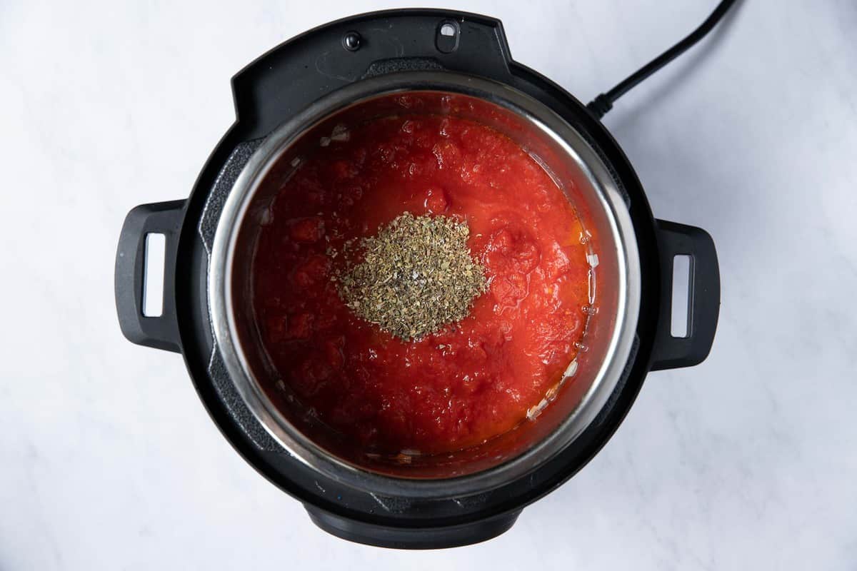 Instant pot with tomato sauce and herbs in center.