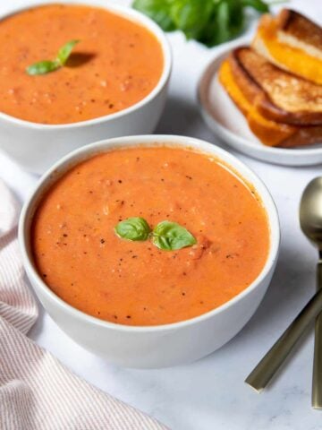 Two bowls of tomato soup with grilled cheese and fresh basil.