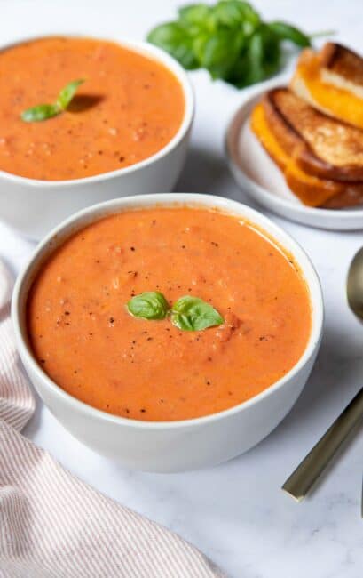 Two bowls of tomato soup with grilled cheese and fresh basil.