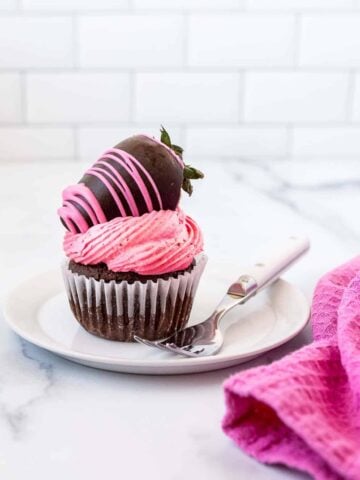 single chocolate cupcake with strawberry frosting and a chocolate covered strawberry on top.