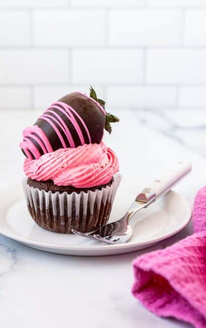 single chocolate cupcake with strawberry frosting and a chocolate covered strawberry on top.