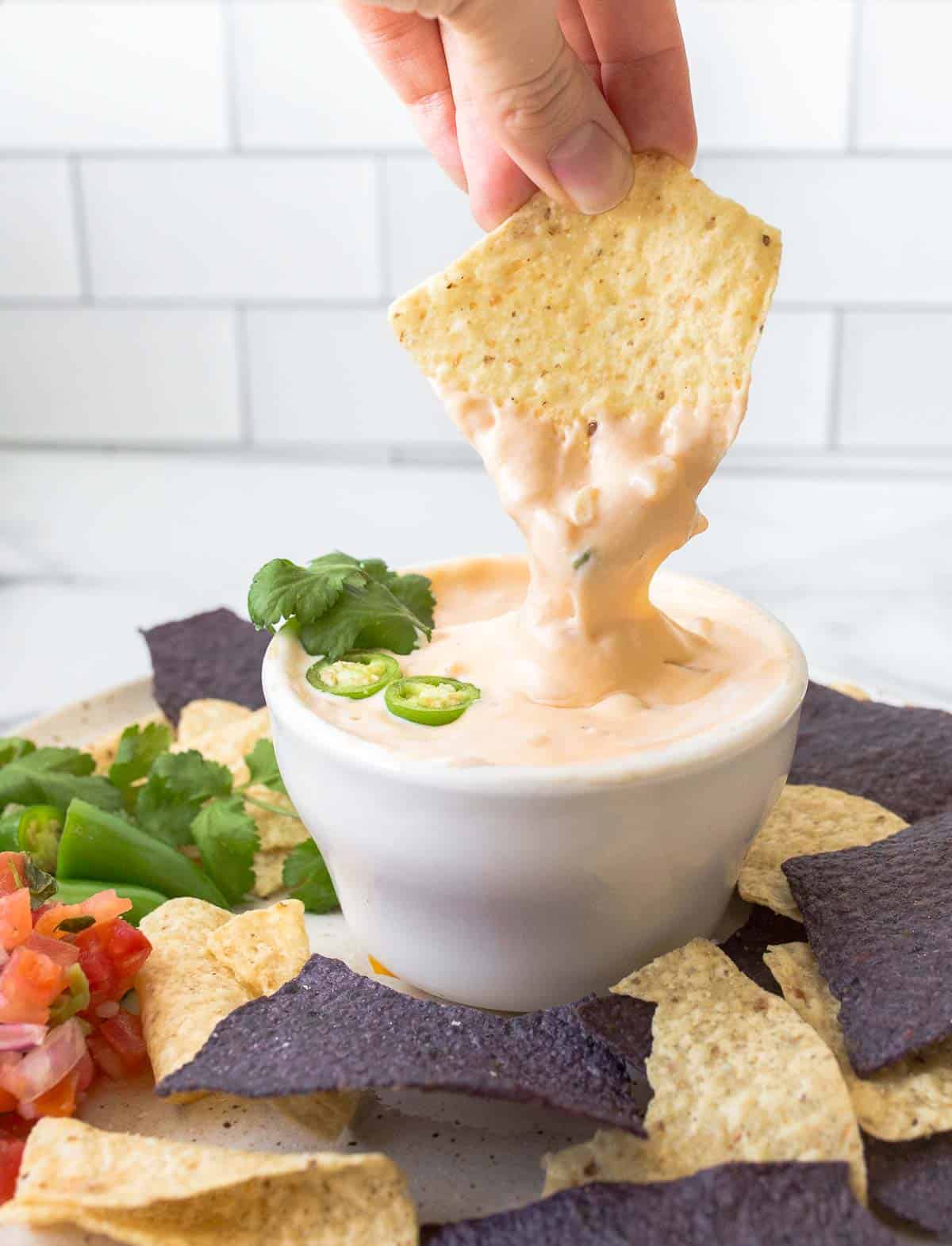 Tortilla chip being dipped into queso with cilantro and pepper garnish.
