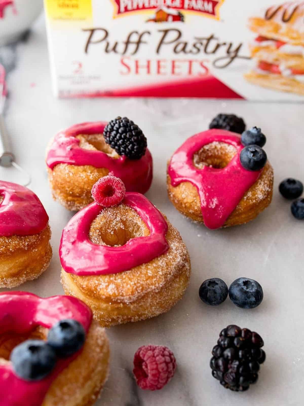 Puff pastry donuts with pink frosting, fresh berries and box of puff pastry in background.
