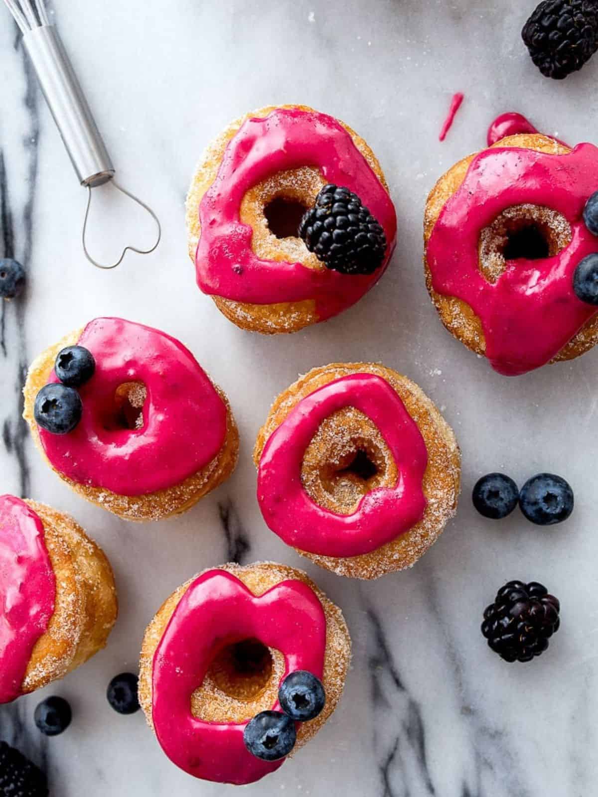 Hot pink donuts decorated with fresh berries on a marble board.