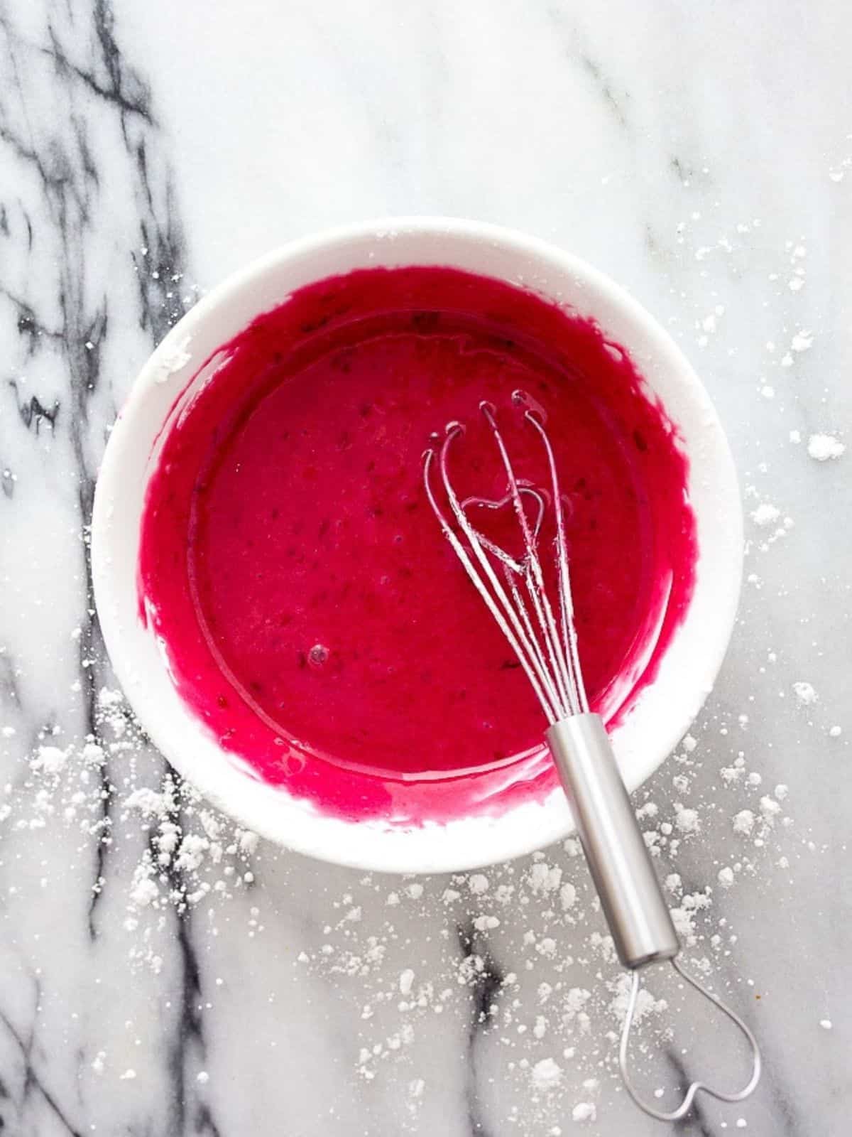 White bowl of hot pink frosting with whisk in it.