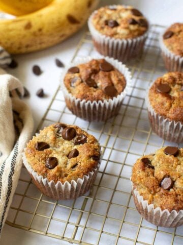 Six almond flour banana muffins with chocolate chips on wire rack.