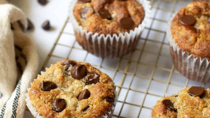 Six almond flour banana muffins with chocolate chips on wire rack.