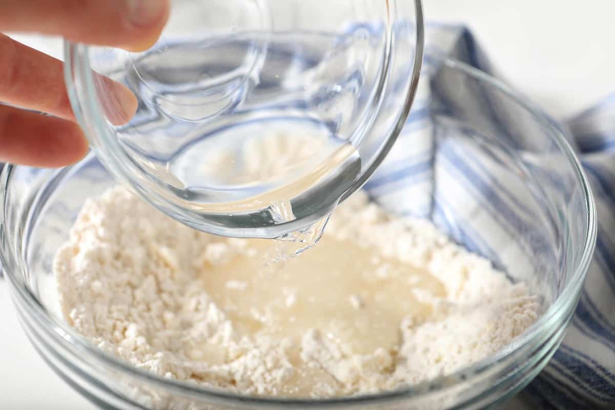 Pouring water and vinegar into pie crust dough.