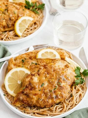 Two plates with chicken over pasta with a lemon garnish.