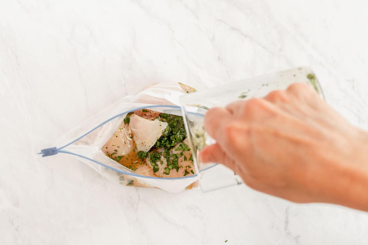 Pouring green marinade over chicken in a bag.