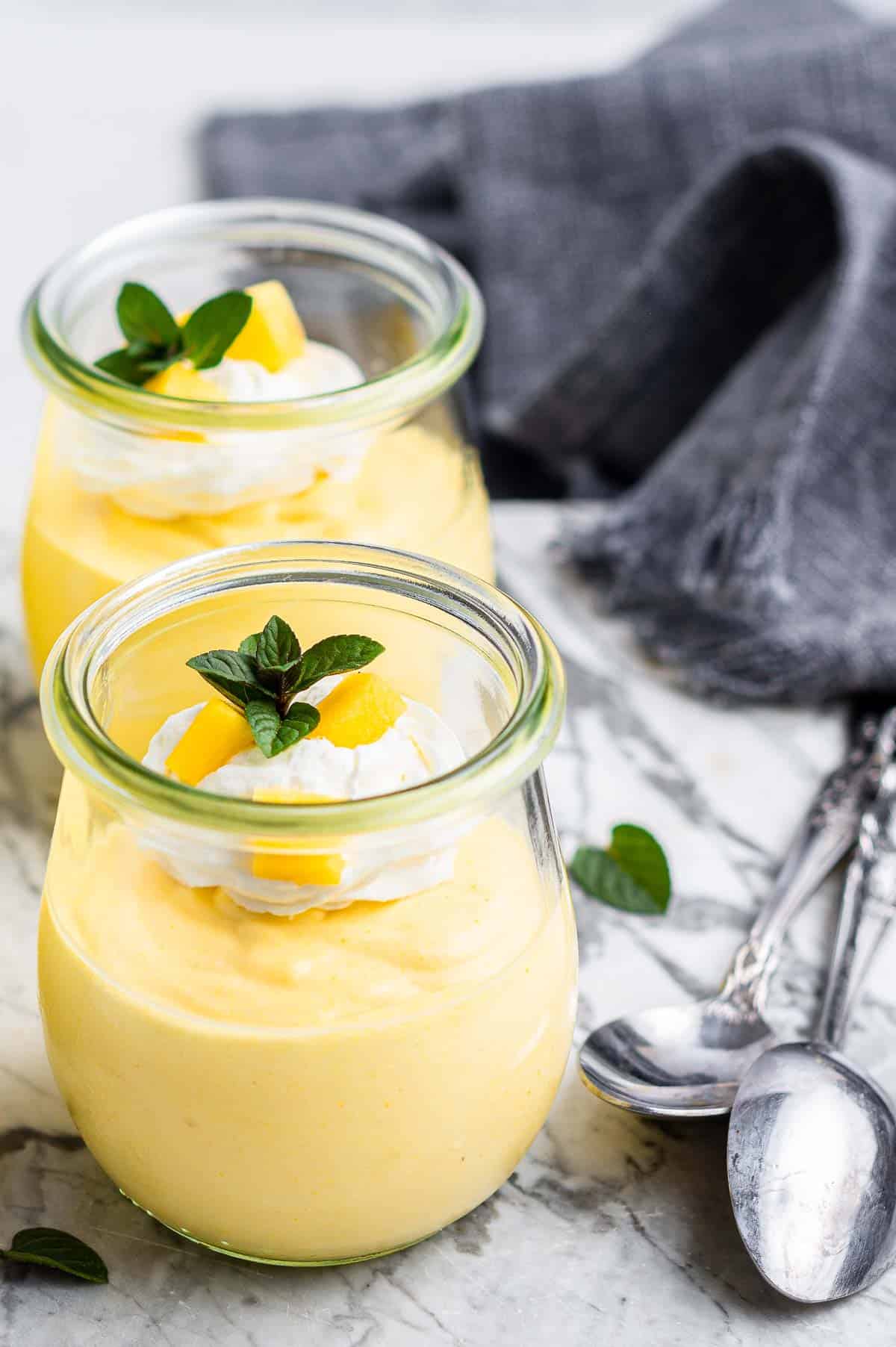 Yellow mango mousse in two jars with spoons on the side.