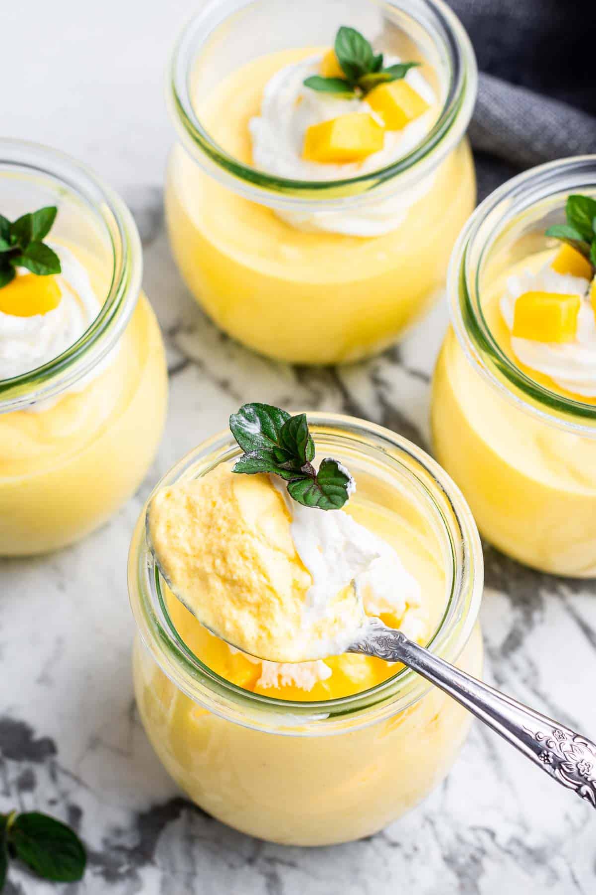 Mango mousse in jars with whipped cream and mint leaf on top.