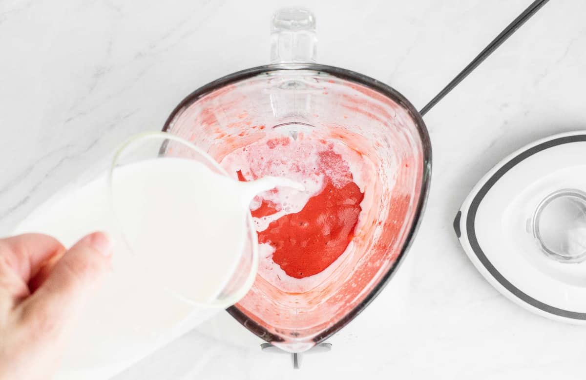 Pouring milk into a blender with strawberries.
