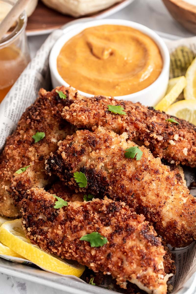 Pile of buttermilk chicken tenders with orange sauce in background.