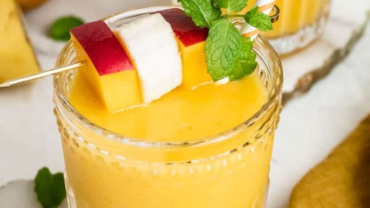 Two glasses of mango banana smoothie garnished with fruit and mint.