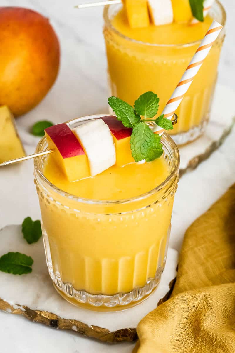 Two glasses of mango banana smoothie garnished with fruit and mint.