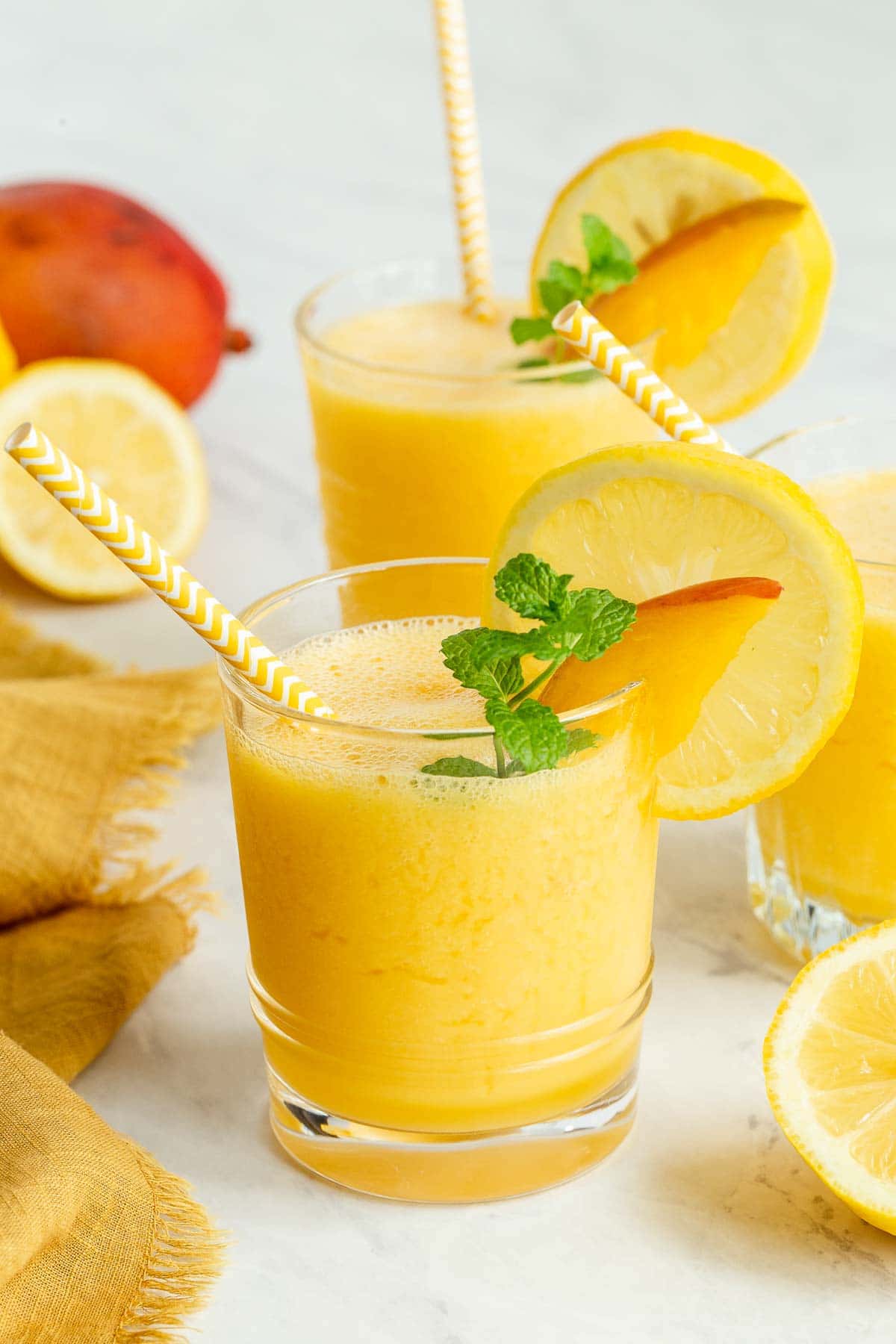 Two glasses of mango lemonade garnished with lemon slices.