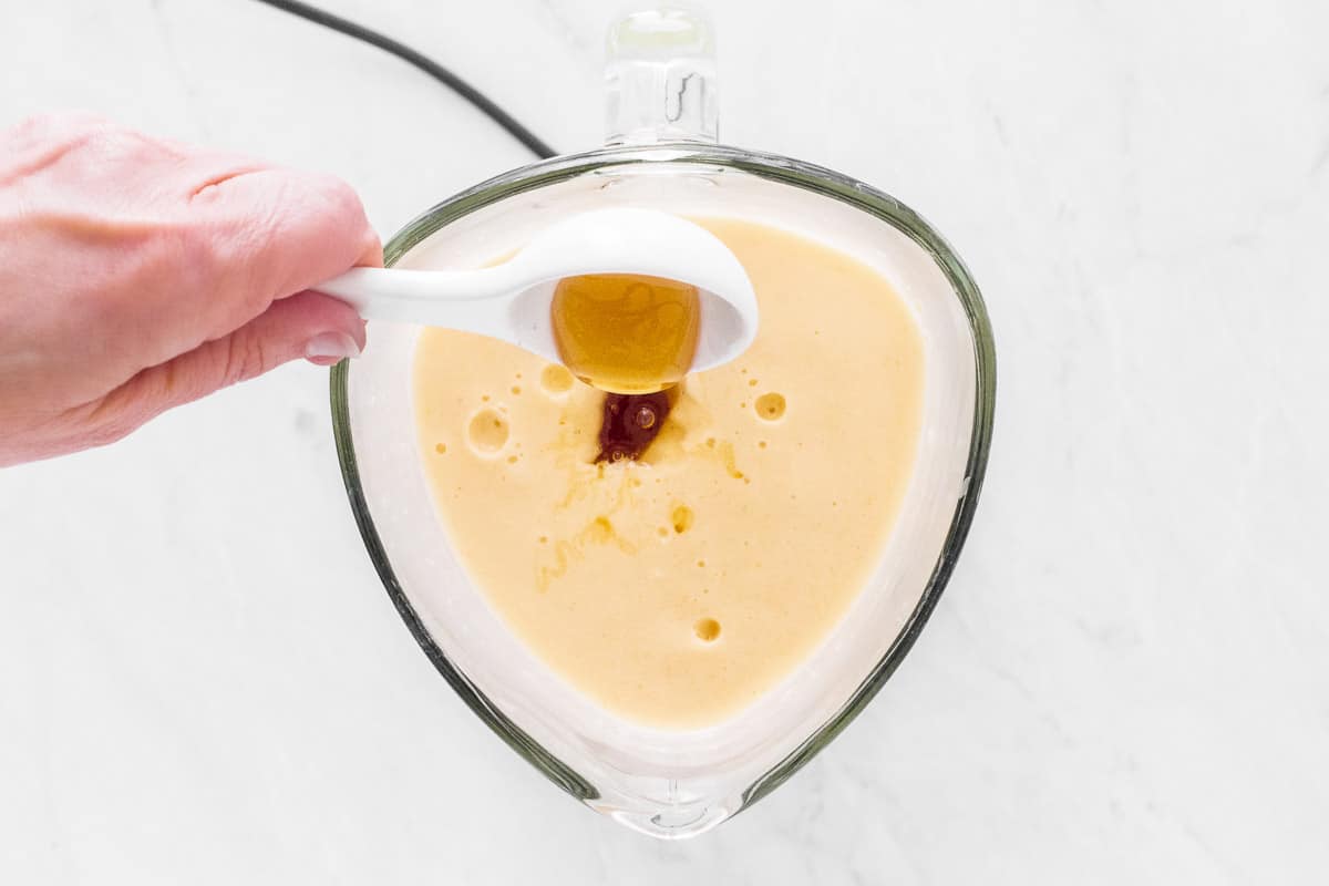Pouring honey into a mango smoothie in the blender.