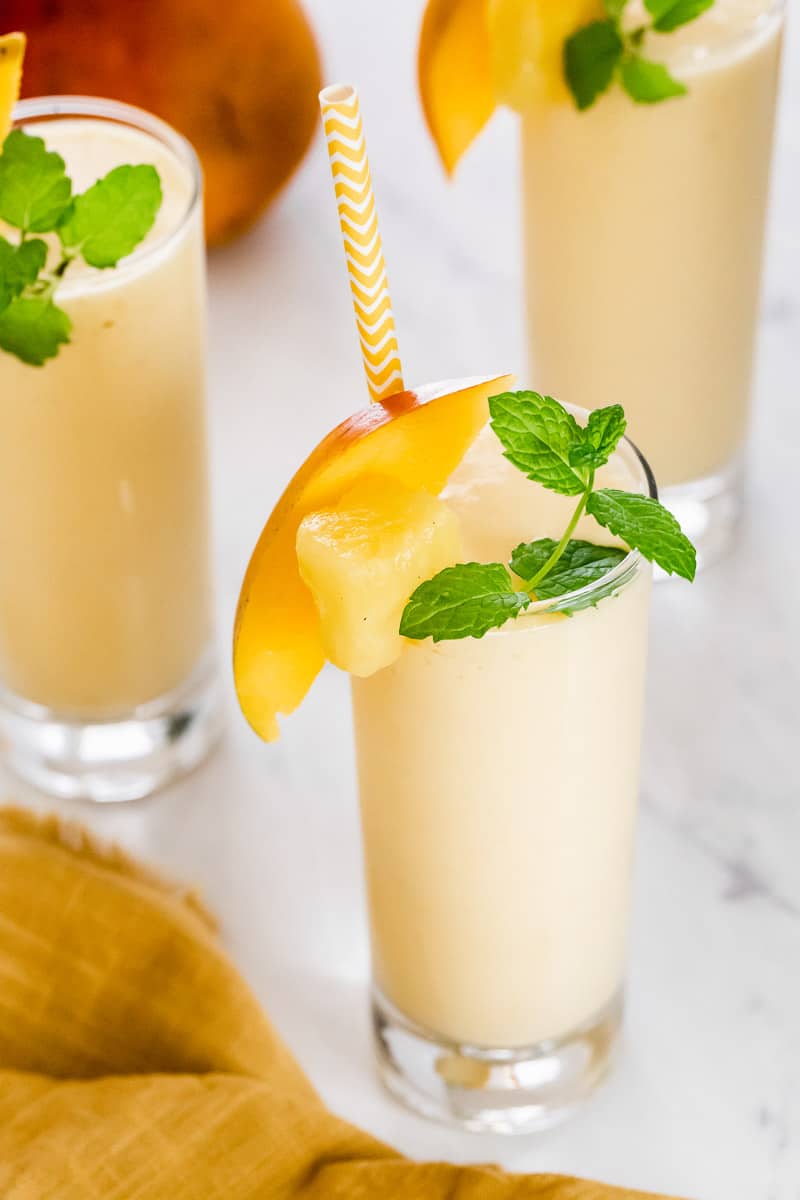 Mango pineapple smoothie in glasses garnished with mint.