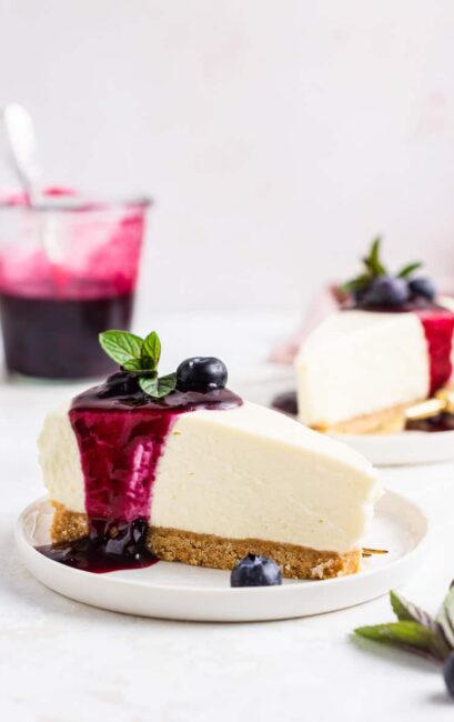 No bake blueberry cheesecake slice drizzled in blueberry sauce on plate.