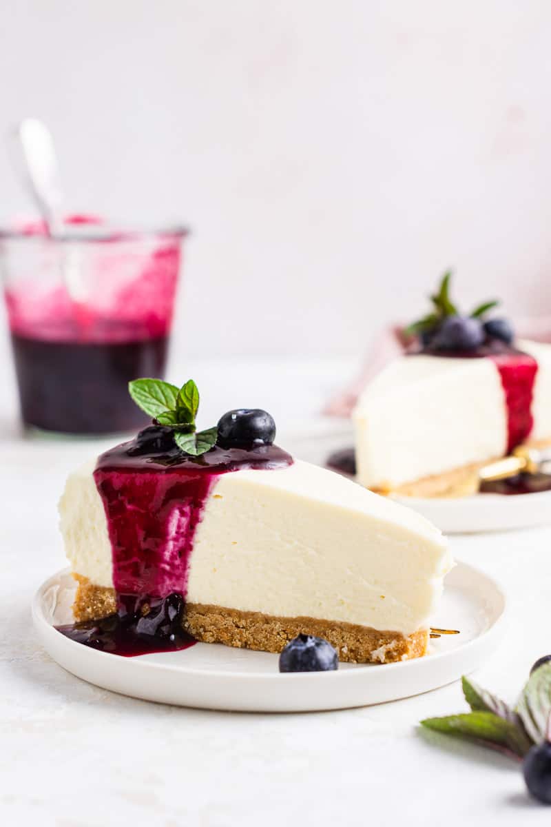 No bake blueberry cheesecake slice drizzled in blueberry sauce on plate.