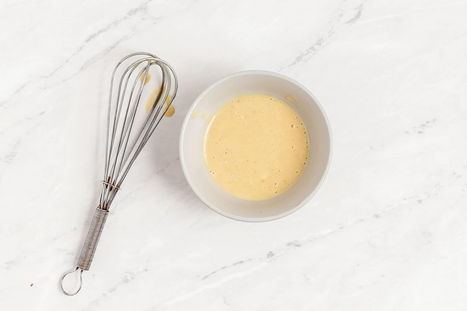 Creamy honey mustard dressing in a small bowl with a whisk.