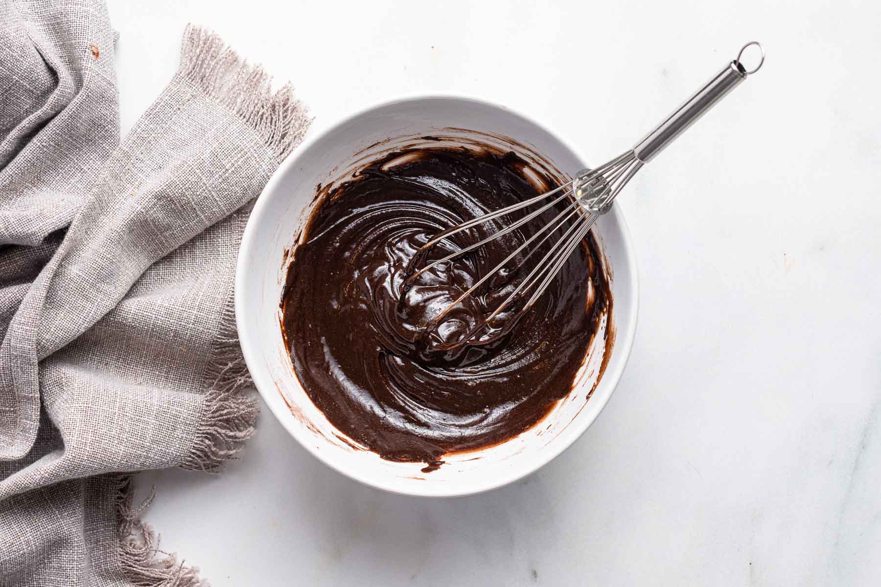 Brownie batter in a white bowl with a large whisk.
