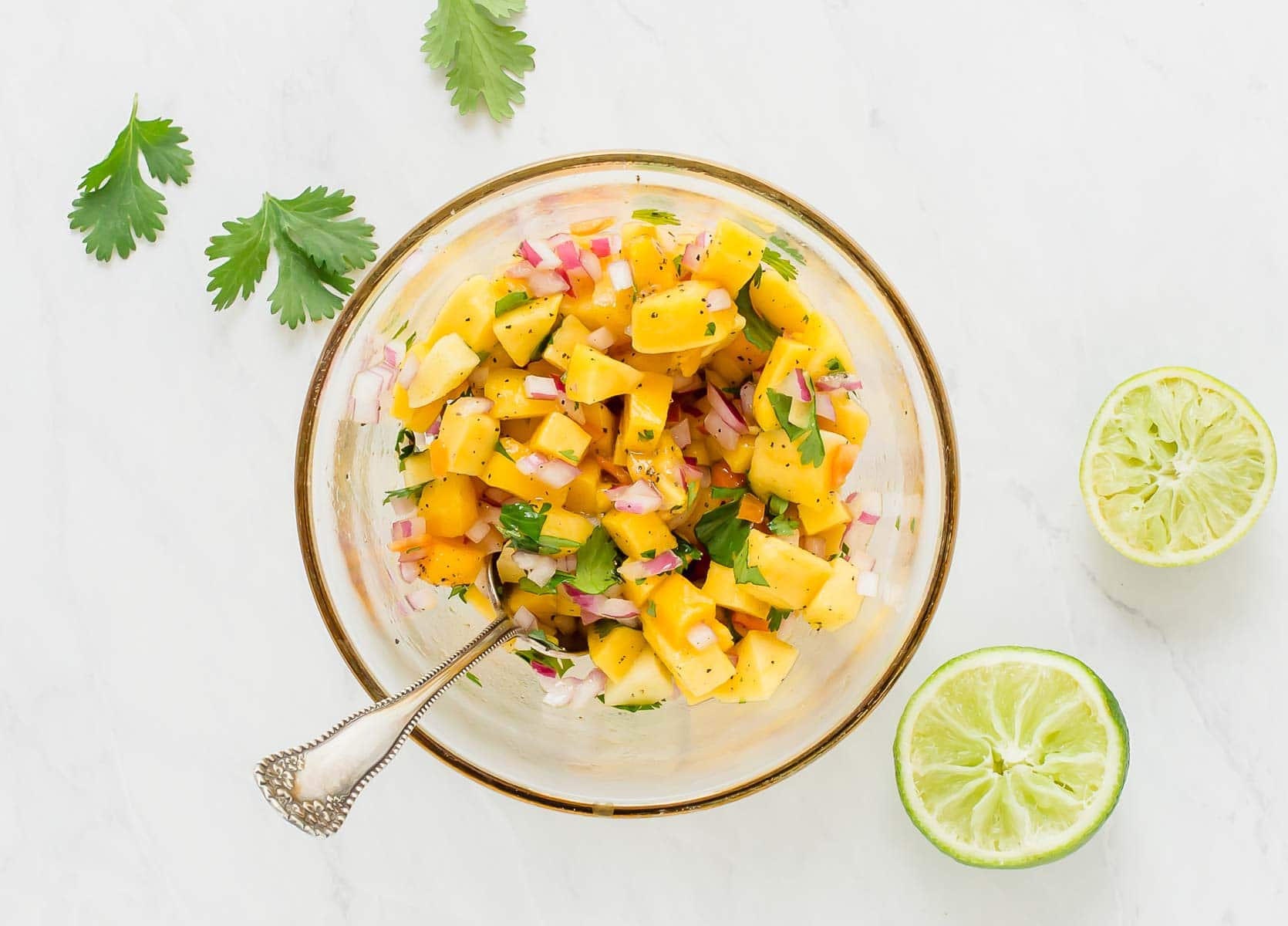 Bright yellow mango habanero salsa in a clear glass bowl with spoon.