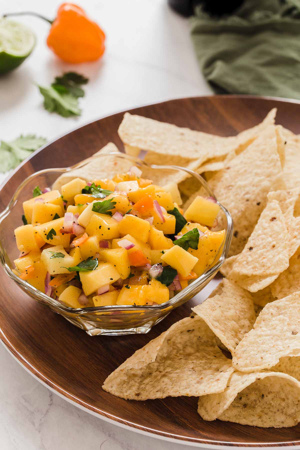 Mango salsa in clear dish with tortilla chips on side.