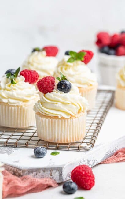 Four white angel food cupcakes on wire rack with fresh berries.