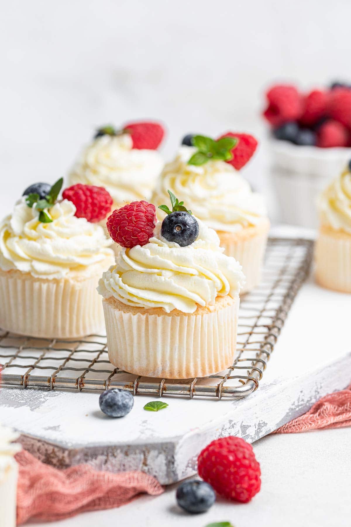 Four white angel food cupcakes on wire rack with fresh berries.