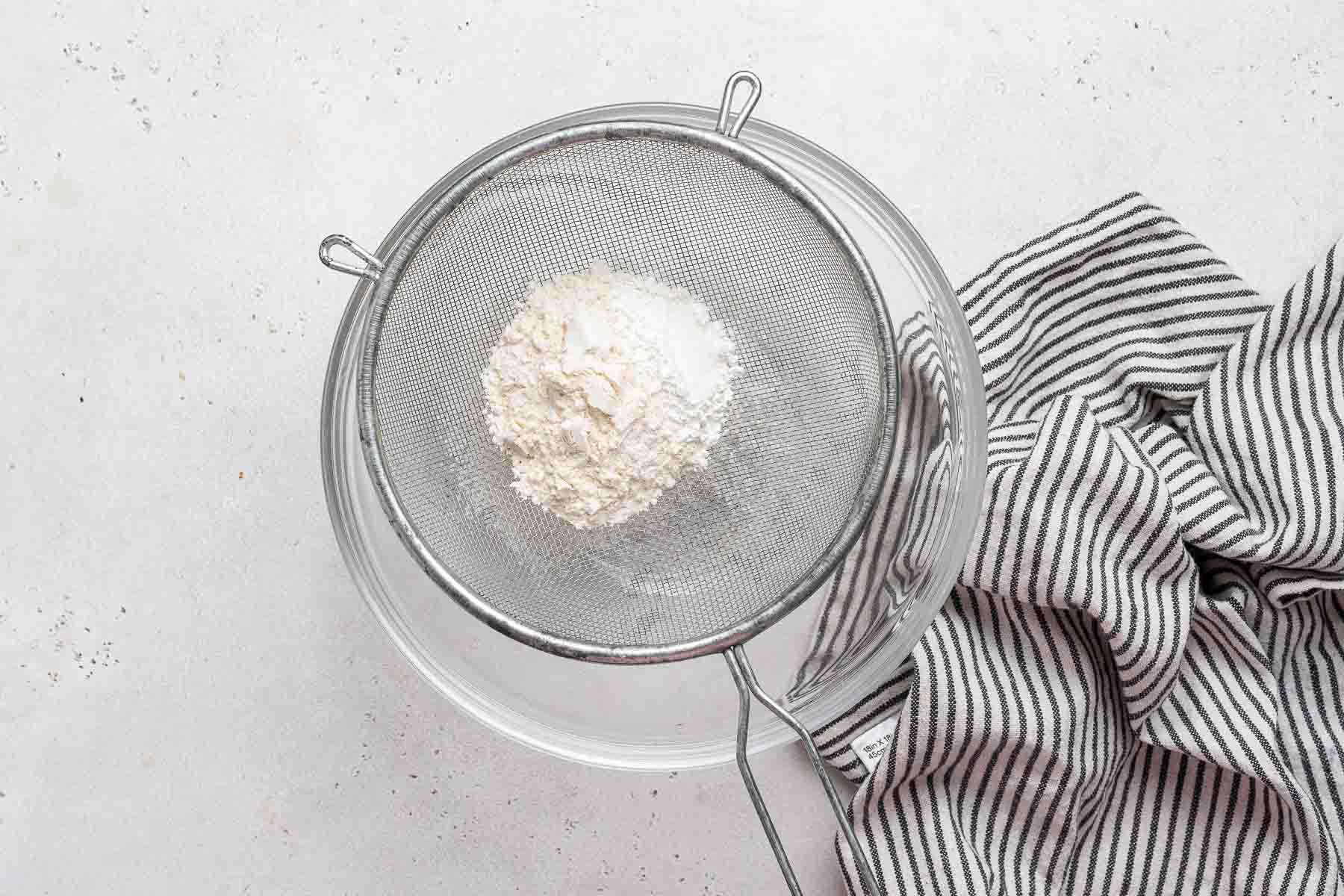 Sifting flour into a clear bowl.