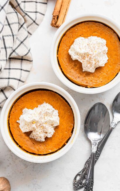 Two ramekins of crustless pumpkin pie with whipped cream and two spoons.