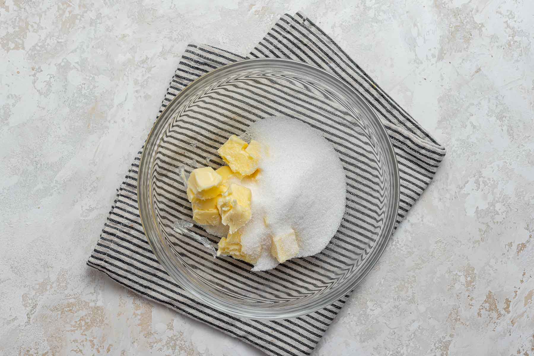 Diced butter and granulated sugar in a clear glass bowl.