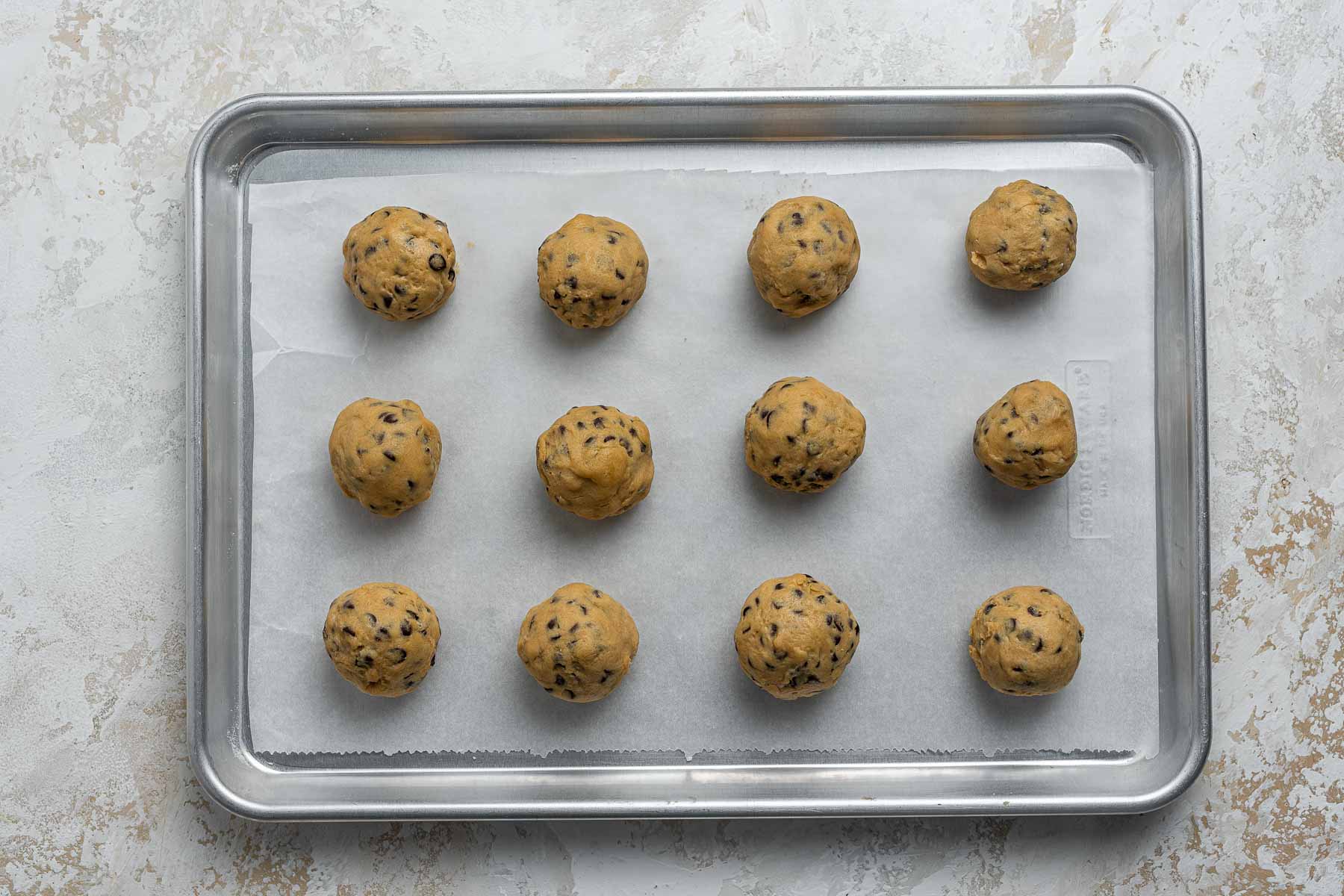 One dozen cookie dough balls on a baking sheet.