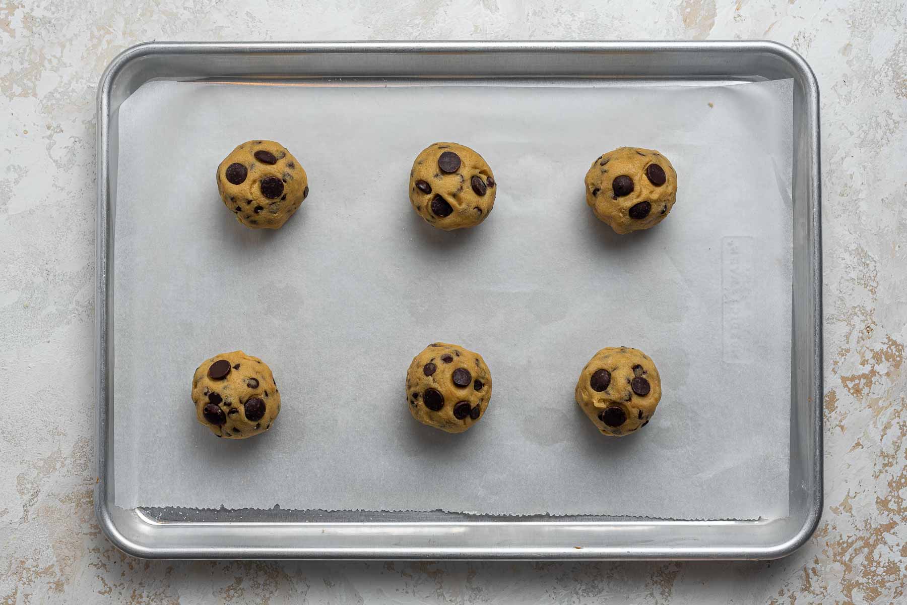 Six dough balls on a baking sheet.
