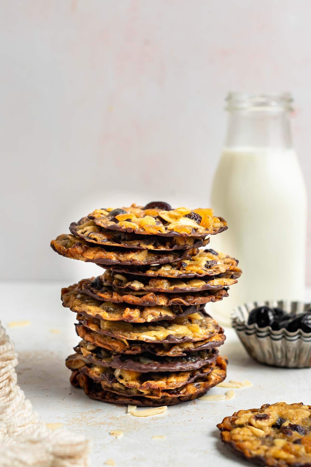 Stack of thin cookies with glass of milk in background.