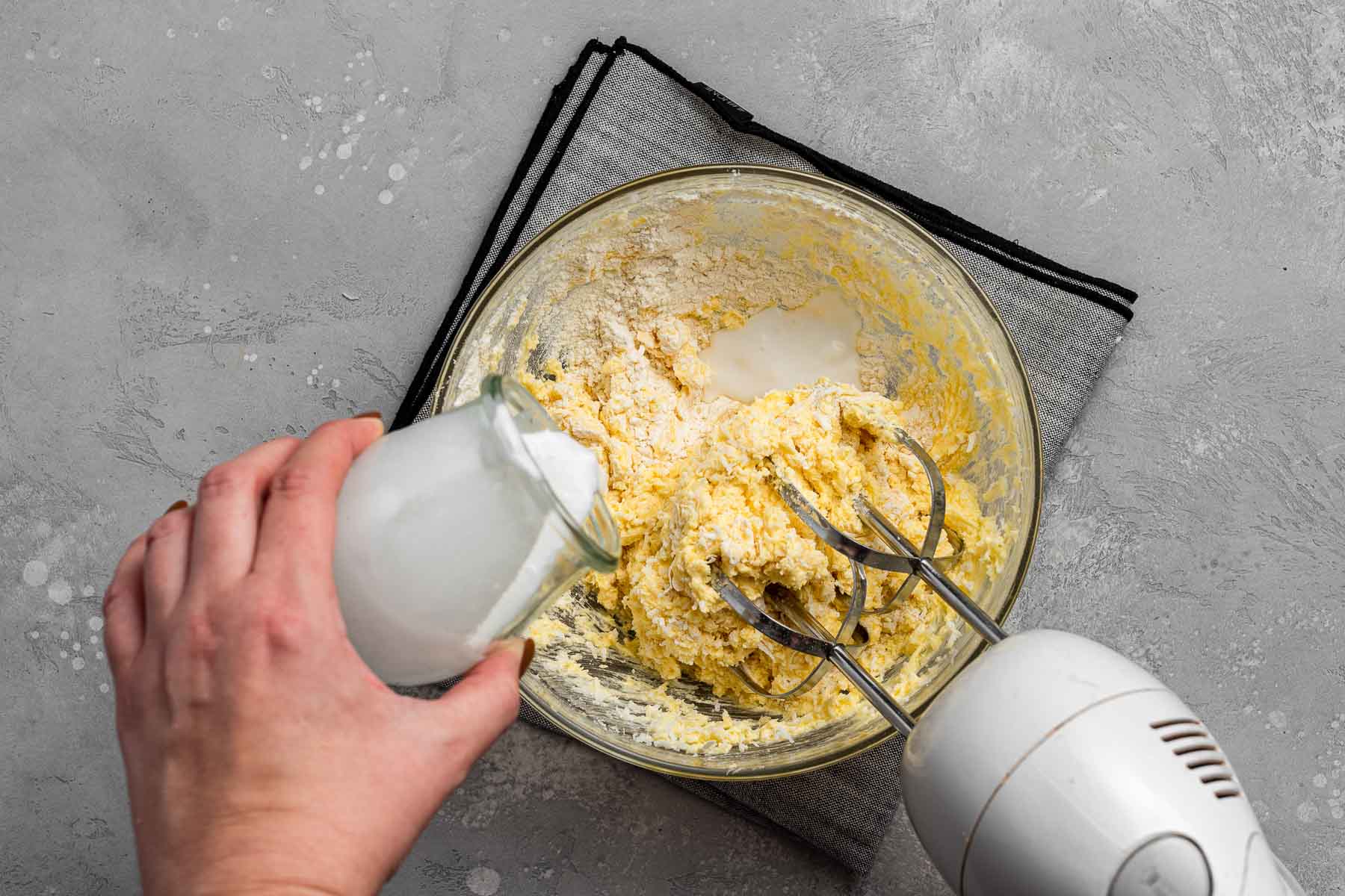 Pouring coconut milk into yellow batter.