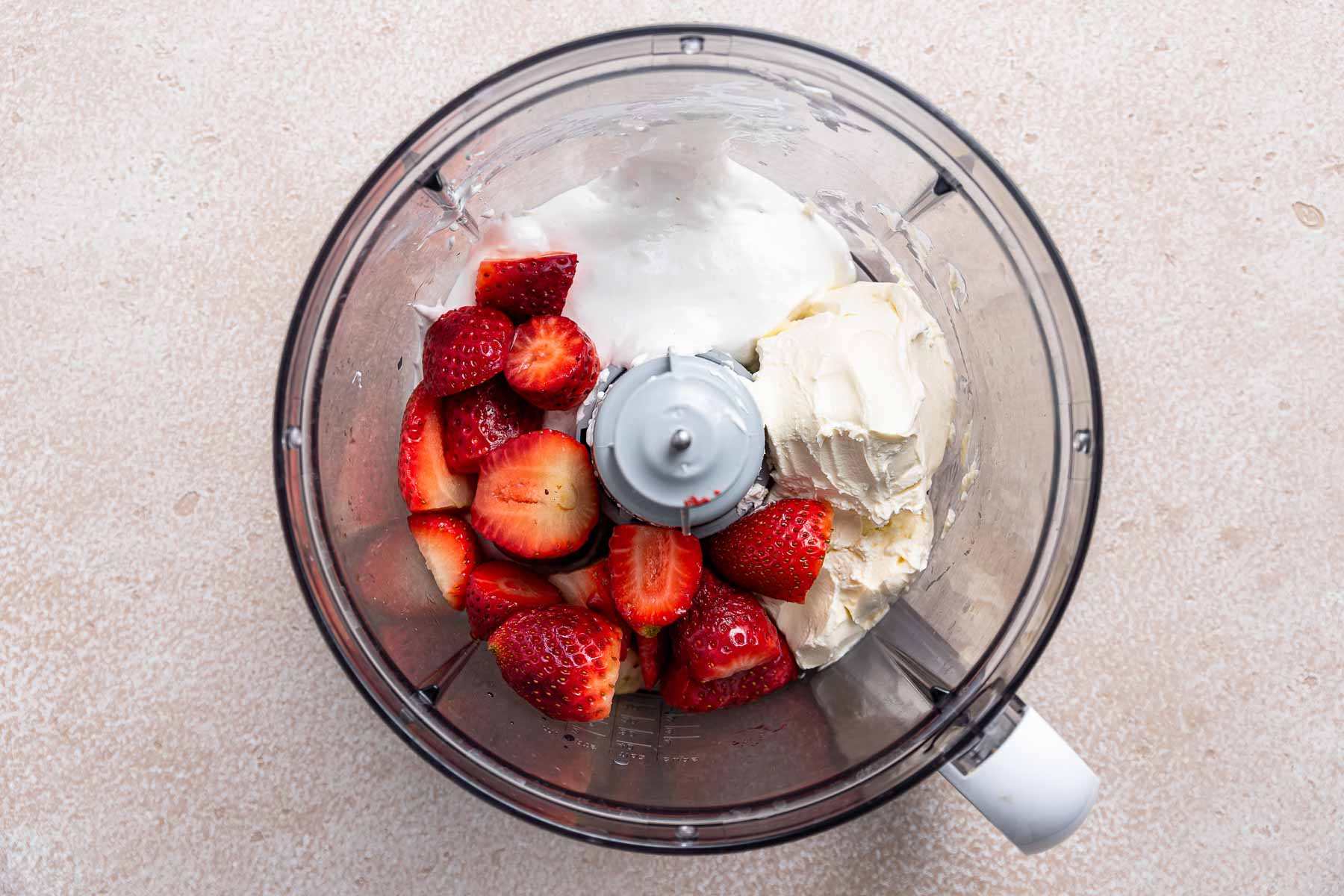 Strawberries and cream in a food processor bowl.