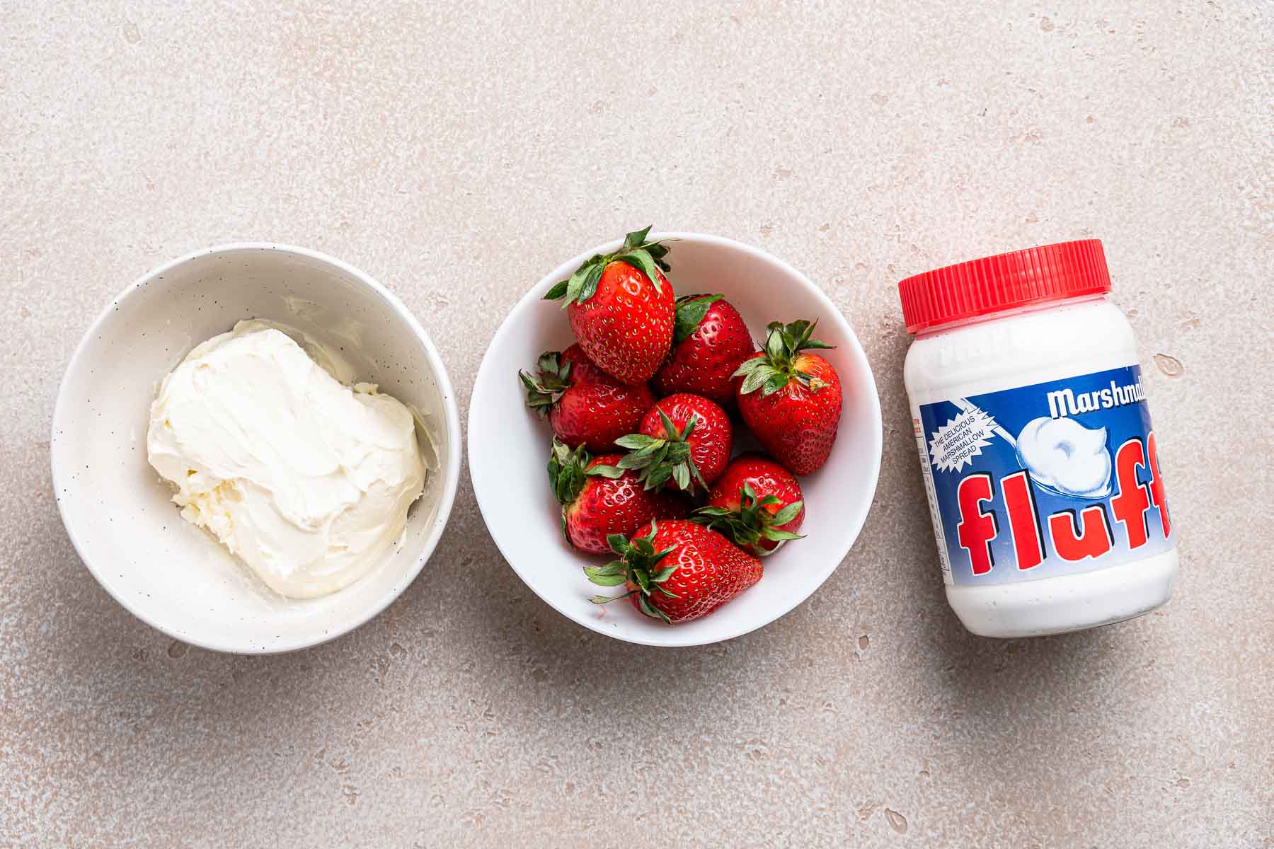 Cream cheese, strawberries, and marshmallow fluff on table.