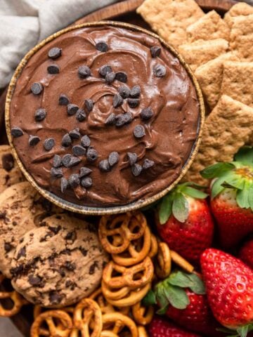 Bowl of chocolate brownie batter dip topped with mini chocolate chips and surrounded by fruit.