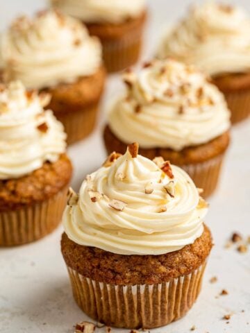 Six carrot cake cupcakes decorated with chopped pecans.