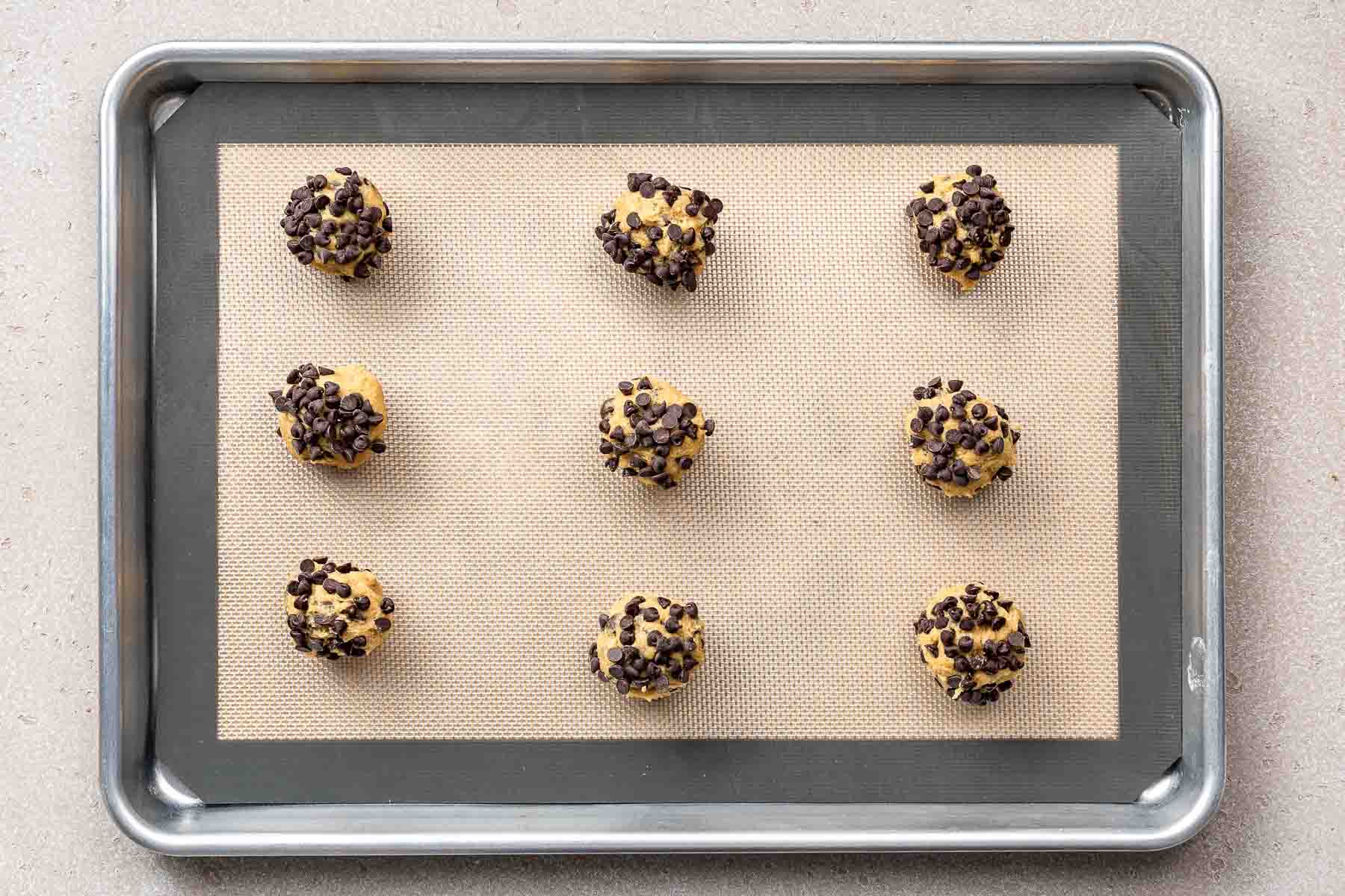 Chocolate chipper cookie dough balls on baking sheet, before baking.