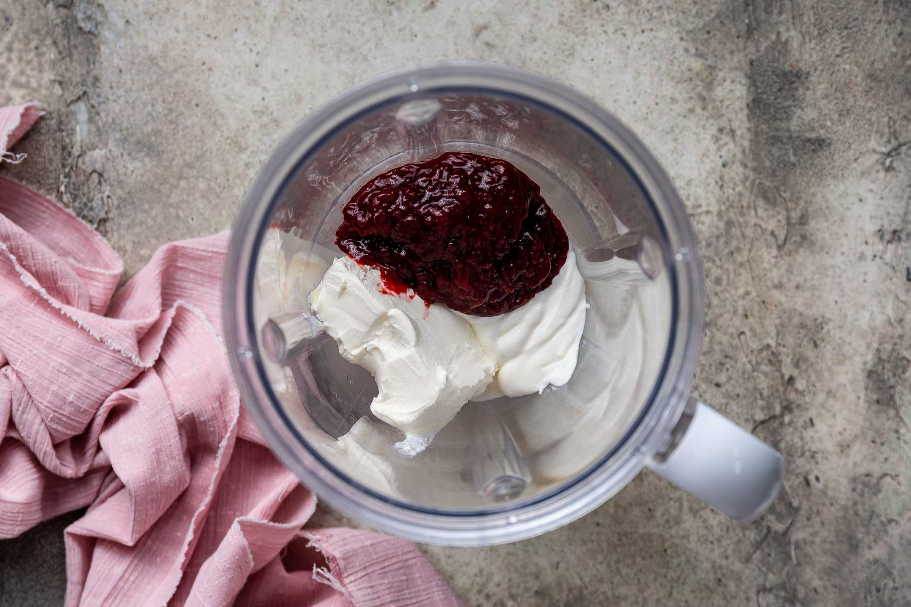 Red jam, sour cream, and cream cheese in the bottom of a blender.