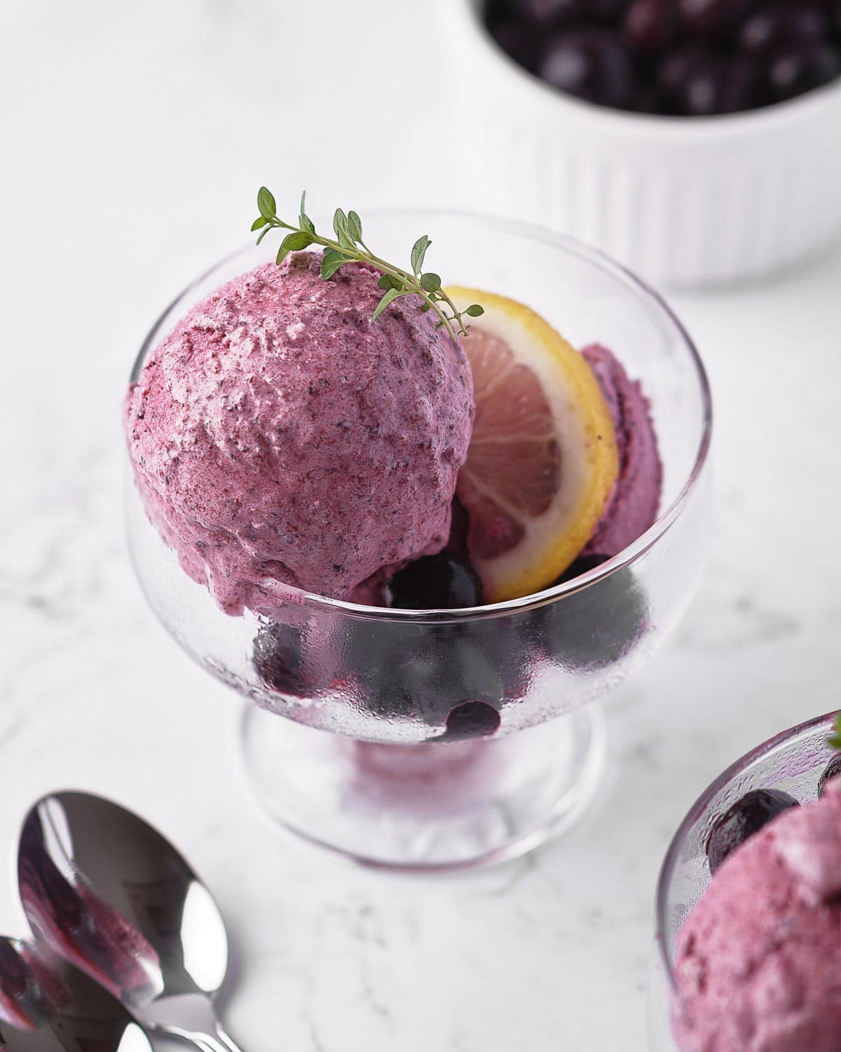 Melting scoop of blueberry sherbet in glass cup.