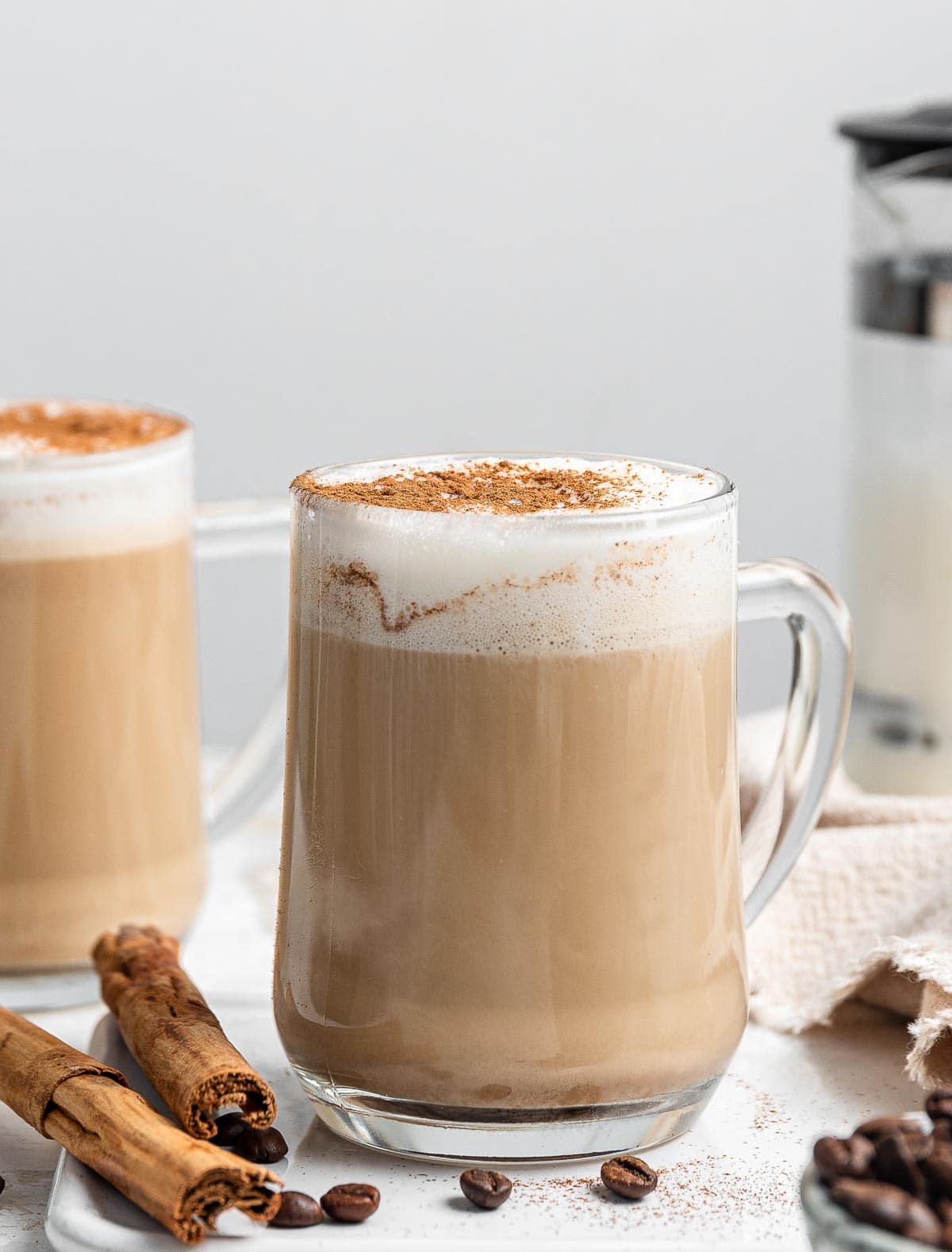 Two mugs of coffee with white foam and cinnamon on top.