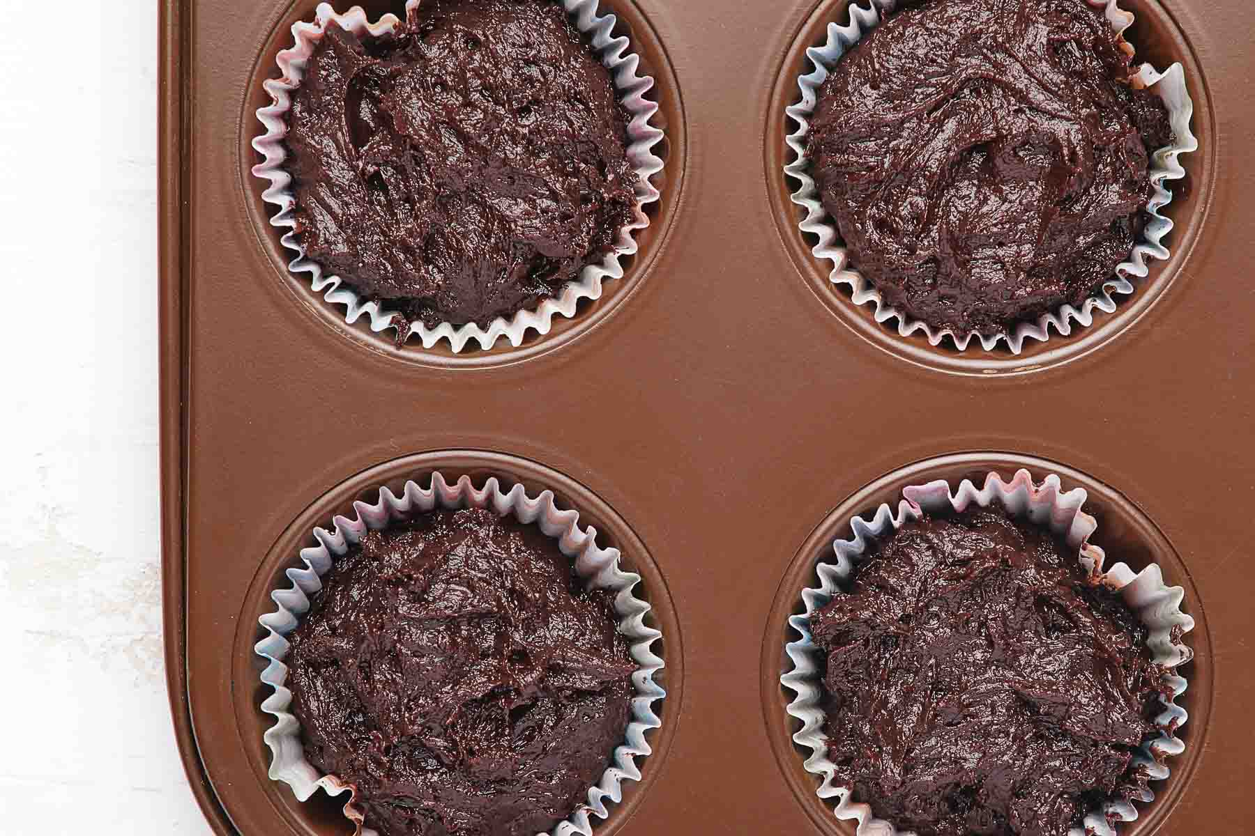 Four chocolate cupcakes, raw before baking.
