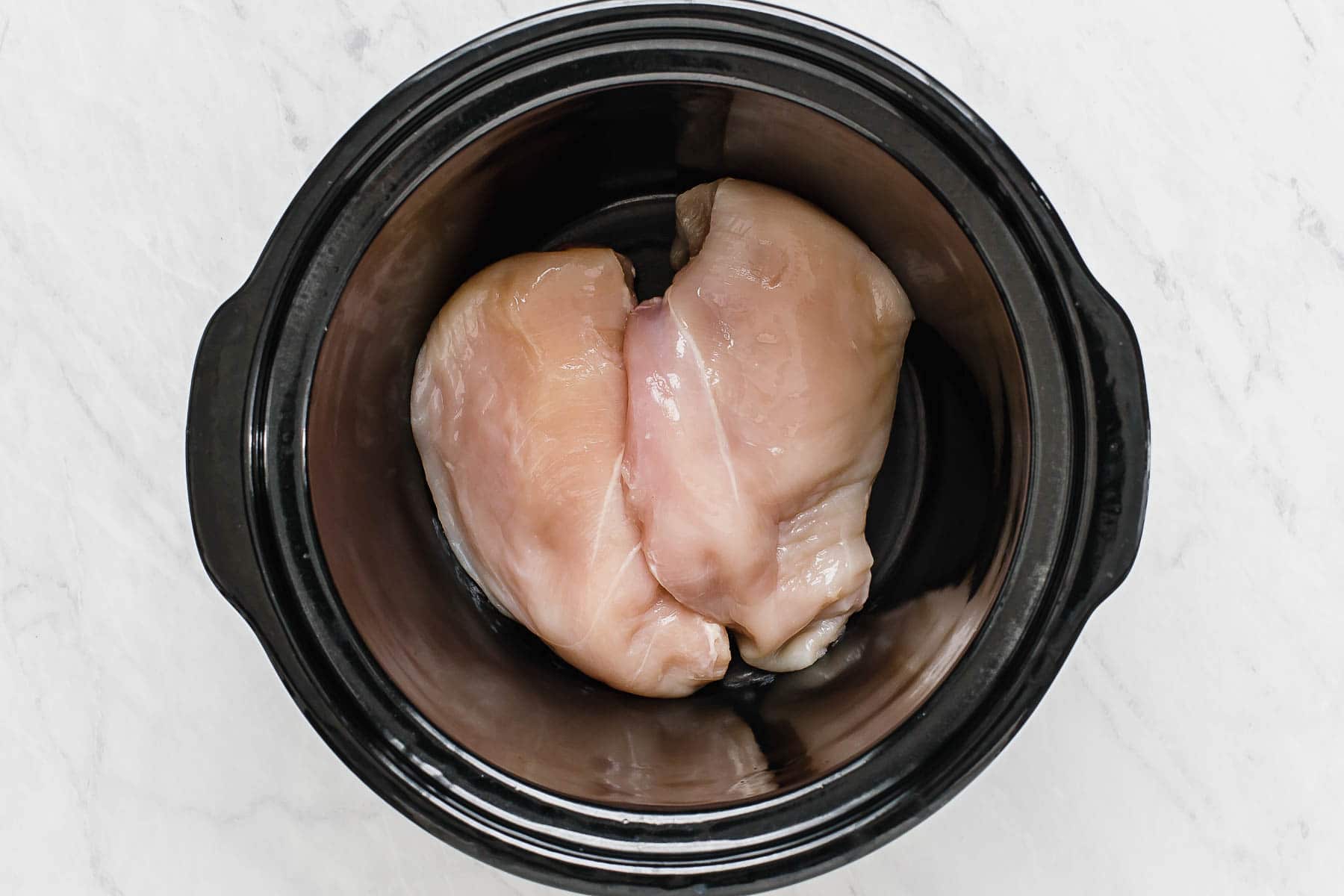 Chicken breasts in black slow cooker.