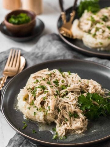 Two plates of shredded chicken over mashed potatoes.